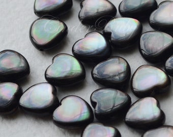 May include: A collection of black heart-shaped beads with iridescent green and purple hues. The beads are made of mother of pearl and are perfect for jewelry making.
