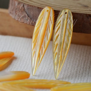 May include: A set of six iridescent yellow shell leaf-shaped pendants. The pendants have a carved design and a hole at the top for stringing.