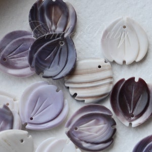 May include: Assortment of purple, white, and brown shell flower-shaped beads with a hole in the center. The beads are carved with a leaf design.