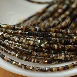 May include: A collection of thin, disc-shaped beads strung together in multiple strands. The beads feature a mix of dark brown, tan, and black tones with iridescent, shimmering green and blue accents throughout the surface of each small bead.