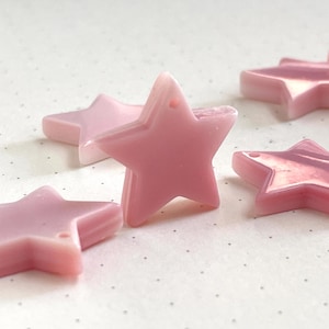 May include: A group of pink star-shaped charms with a shiny, iridescent finish. The charms have a hole in the top for stringing or attaching.