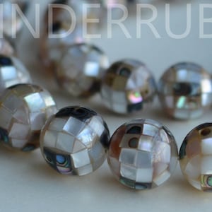 May include: A strand of iridescent white and brown shell beads, each bead is made of many small squares of shell, creating a mosaic effect.