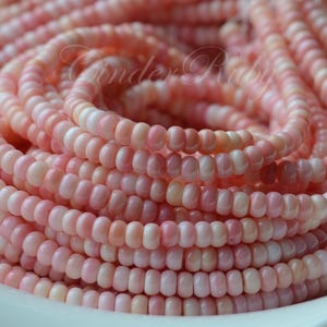 May include: A strand of pink and white shell beads. The beads are small and round, and they are strung together on a clear thread.