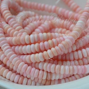 May include: A strand of pink and white shell beads. The beads are small and round, and they are strung together on a clear thread.