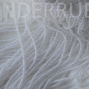 May include: A close-up of a pile of white seed beads. The beads are small and round, and they are arranged in a random pattern.