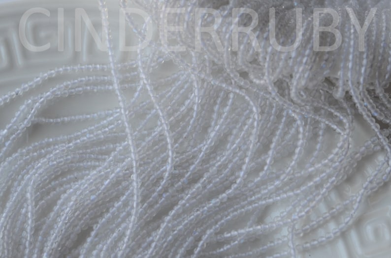 May include: A close-up of a pile of white seed beads. The beads are small and round, and they are arranged in a random pattern.