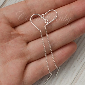 May include: Silver heart shaped earrings with a delicate chain dangling from each heart. The chains are connected to a small bar at the bottom.