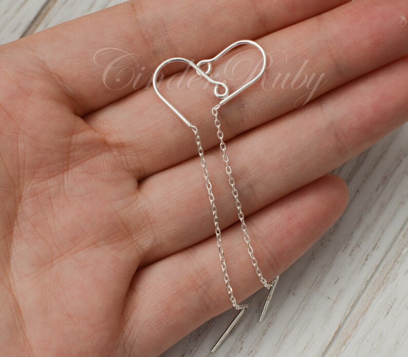 May include: Silver heart shaped earrings with a delicate chain dangling from each heart. The chains are connected to a small bar at the bottom.