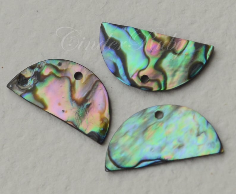 May include: Three iridescent abalone shell half-circle pendants with holes for hanging. The shells have a variety of colors, including green, blue, purple, and brown.