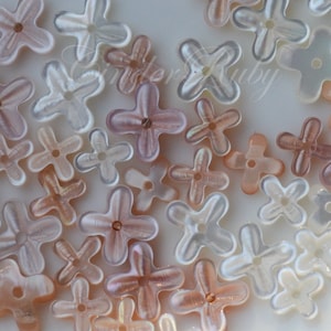 May include: A collection of iridescent, pastel pink and white flower-shaped beads. The beads are made of a smooth, pearlescent material and have a hole in the center for stringing.