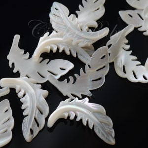 May include: A collection of white mother of pearl shell leaf charms. The leaves are intricately carved with a delicate pattern and have a subtle iridescent sheen.
