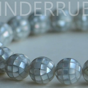 May include: A white bracelet made of round, iridescent beads with a geometric pattern. Each bead has a slightly different pattern.