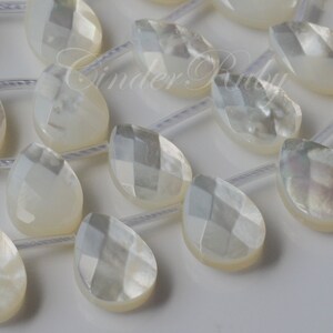 May include: A strand of white mother of pearl teardrop beads with a faceted design. The beads are strung on a clear elastic cord.
