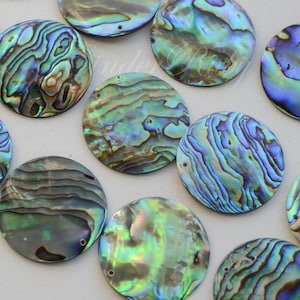 May include: Assortment of round iridescent abalone shell pieces with a green, blue, and purple color scheme. The shells have a natural, organic texture and are perfect for crafting projects.