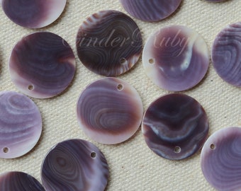 May include: A collection of round, flat, purple and white shell beads with a hole drilled through each. The beads have a swirling pattern and are arranged on a neutral-colored surface. These beads are suitable for jewelry making.