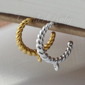 May include: Two twisted hoop earrings, one gold and one silver. The earrings are hanging from a book.