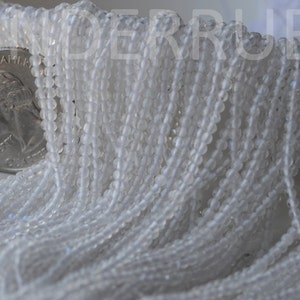 May include: A strand of white glass beads, approximately 4mm in diameter. The beads are translucent and have a slight iridescent sheen. The beads are strung on a clear thread and are arranged in a loose, flowing pattern.