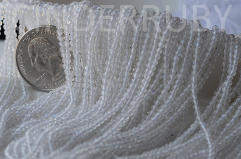 May include: A strand of white glass beads, approximately 4mm in diameter. The beads are translucent and have a slight iridescent sheen. The beads are strung on a clear thread and are arranged in a loose, flowing pattern.