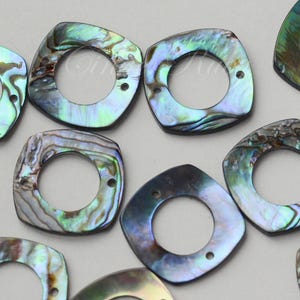 May include: A group of 10 iridescent abalone shell square-shaped beads with a hole in the center. The beads have a dark blue, green, and purple iridescent sheen.