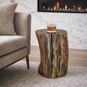 May include: A rustic, wooden side table with a natural, organic shape. The table is made from a section of a tree trunk, featuring a split down the center. A glass of amber liquid with ice sits on top. The table is approximately 18 inches tall.