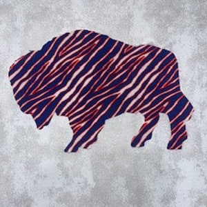 May include: A blue and red striped buffalo silhouette cutout. The buffalo is facing right and has a white background.
