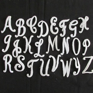 May include: White felt letters of the alphabet in a cursive font. The letters are arranged in alphabetical order.