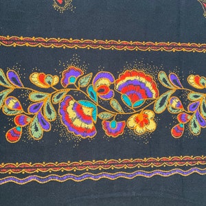 May include: Black fabric with a repeating floral pattern. The design features colorful flowers in shades of red, purple, yellow, and green, with a detailed border in orange and purple. The fabric has a vintage aesthetic.