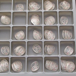 May include: A white plastic tray with 25 compartments, each containing a stack of white lace appliques with embroidered letters. The letters are in a variety of fonts and styles.