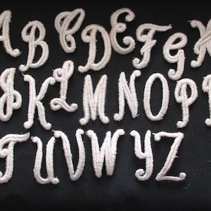 May include: White felt letters of the alphabet in a cursive font. The letters are arranged in alphabetical order.