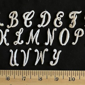 May include: White felt letters of the alphabet in a cursive font. The letters are arranged in two rows, with the first row containing the letters A through G and the second row containing the letters K through R. The letters U, V, W, and Y are in a third row. The letters are approximately 1 inch tall.