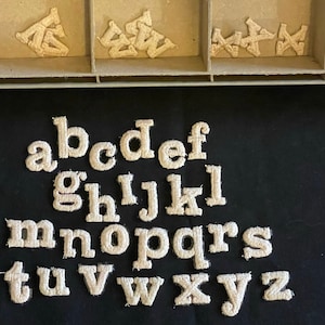 May include: A set of white felt letters of the alphabet, a through z, on a black background.