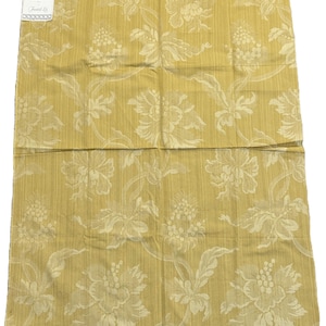 May include: A rectangular piece of mustard yellow fabric featuring a tonal floral damask pattern. A small white rectangular tag is attached to the top left corner, displaying the text Pierre Frey and Fontill Ltd in a clear, legible font.