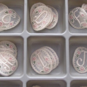 May include: Nine white lace appliques with embroidered letters and floral designs. The letters are I, J, L, D, E, and F.