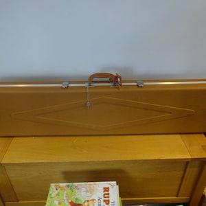 May include: A vintage, mustard-colored hard case with a brown leather handle and silver-toned latches. The case has a diamond-shaped design on the front and a key hanging from the handle. It rests on a wooden chest.