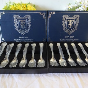 May include: Two blue boxes with gold trim containing a set of 12 silver teaspoons. The boxes have the text "1907 - 2017 Set of the Commemorative Teaspoons Celebrating 110 Years of Dragons"