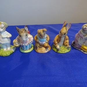 Puede incluir: Colección de cinco figuras de cerámica que representan animales antropomórficos. Las figuras incluyen un gato, un ratón, un conejo y un erizo, cada uno con ropa detallada y sentado sobre una pequeña base de hierba. Las figuras están pintadas en varios colores.