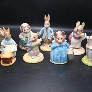 May include: A set of ceramic figurines featuring animal characters in detailed outfits. The figurines, including rabbits and mice, are painted in bright colours. Each character has a unique pose and is set on a small base, creating a charming display.