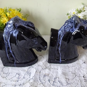 Op de afbeelding: Set van zwarte keramische boekensteunen in de vorm van een paardenkop met blauw-witte accenten. De boekensteunen zijn ontworpen om rechtop te staan. Decoratieve woonaccessoires.