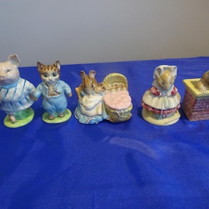 May include: A collection of five ceramic figurines featuring animal characters. The figurines include a pig, a cat, a rabbit with a cradle, a mouse, and a fox in a chimney. Each figure is painted with bright colors and detailed clothing.