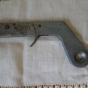 Può includere: Un accendino in metallo argentato a forma di pistola con un grilletto e un foro rotondo sul lato. L'accendino ha la parola "SOC" in rilievo sulla parte superiore.