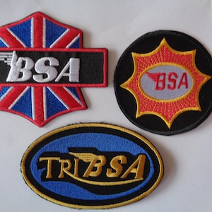 Peut inclure: Trois patchs brodés représentant le logo BSA. Le premier patch est un Union Jack rouge, blanc et bleu avec une bannière noire au milieu qui indique "BSA" en blanc. Le deuxième patch est un cercle noir avec une étoile rouge et un ovale blanc au centre qui indique "BSA" en rouge. Le troisième patch est un ovale avec un fond bleu et une bordure dorée. Le texte "TRIBSA" est en or avec un logo ailé doré.