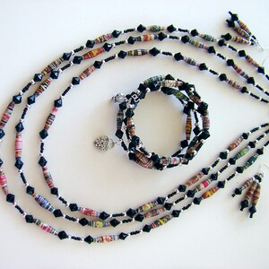 May include: A multi-strand necklace and matching earrings made of black and colorful paper beads. The necklace is layered with black beads and the paper beads are rolled and have a multi-colored pattern. The earrings are a simple drop style with a single paper bead.