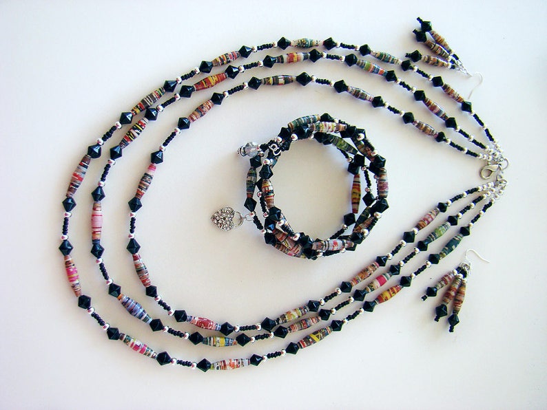 May include: A multi-strand necklace and matching earrings made of black and colorful paper beads. The necklace is layered with black beads and the paper beads are rolled and have a multi-colored pattern. The earrings are a simple drop style with a single paper bead.