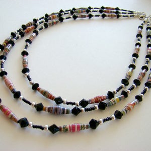 May include: A three-strand necklace with black and multi-colored paper beads and black faceted beads.