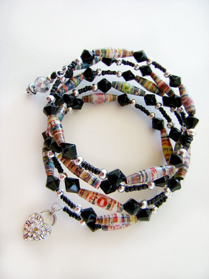 May include: Multi-strand bracelet with black beads, silver beads, and colorful paper beads. The bracelet has a heart-shaped charm with rhinestones.