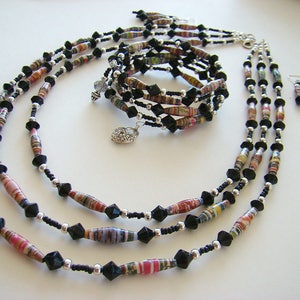 May include: A multi-strand necklace made of black and colorful paper beads with silver accents. The necklace is layered and features a variety of bead shapes and sizes.