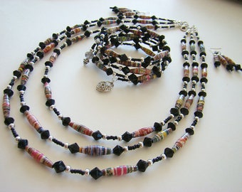 May include: A multi-strand necklace made of black and colorful paper beads with silver accents. The necklace is layered and features a variety of bead shapes and sizes.
