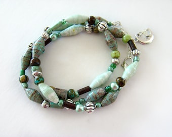 Può includere: Una collana multifilo con perline verdi, marroni e argentate. La collana presenta un ciondolo a forma di luna crescente.