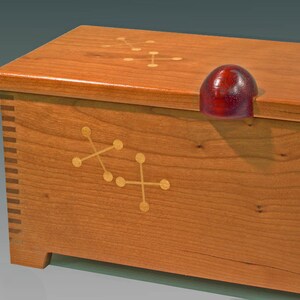 May include: A wooden box with a cherry finish and a red knob. The box has a geometric design inlaid in the wood.