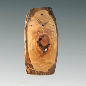 May include: A wooden clock with a natural wood finish. The clock face is made from a tree trunk slice with a knot hole in the center. The clock hands are black and gold.